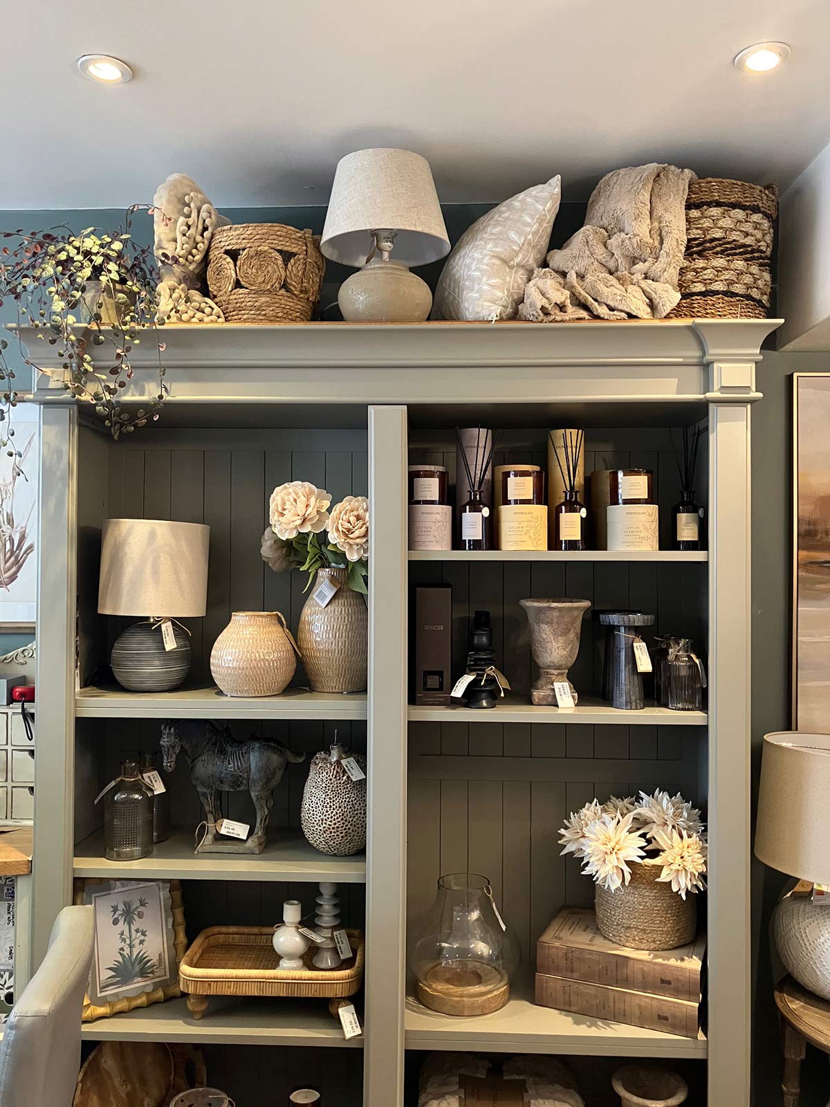 A bookshelf containing a number of lovely decor items, including vases, lamps, scented diffusers, ornaments, and artificial flowers.